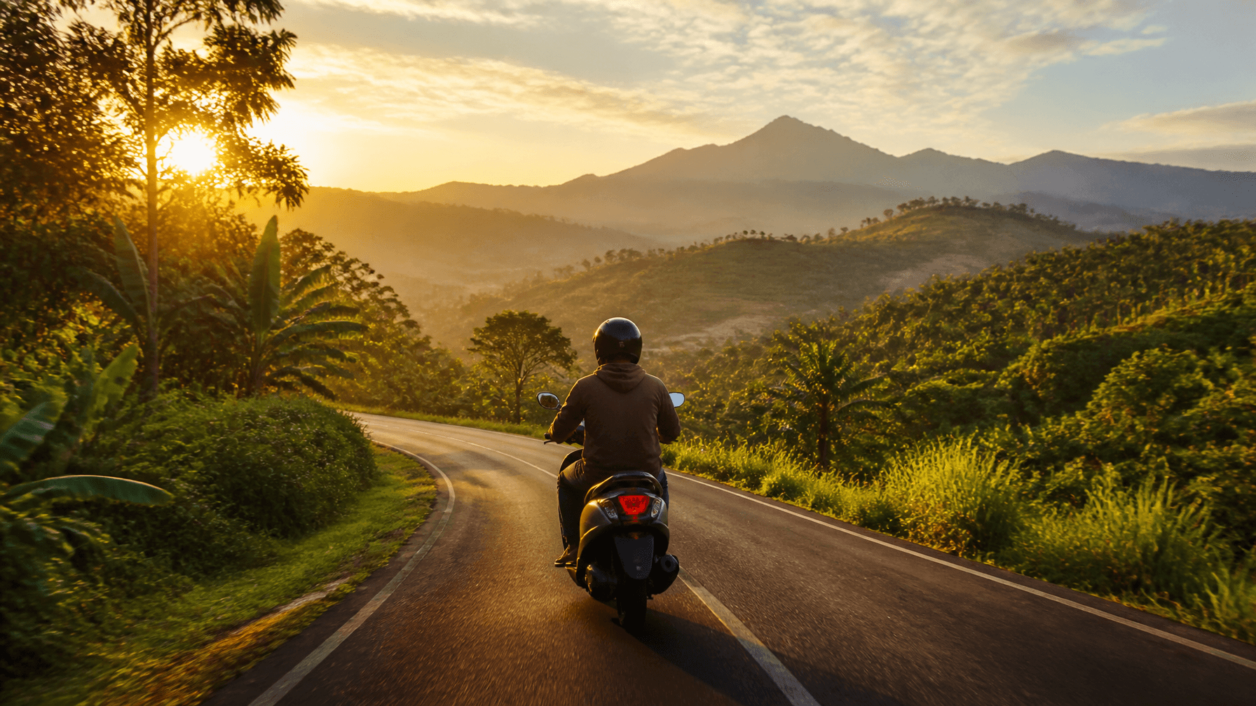 A vibrant, cinematic photo of a person riding a scooter on a winding, lush green road in the hills s