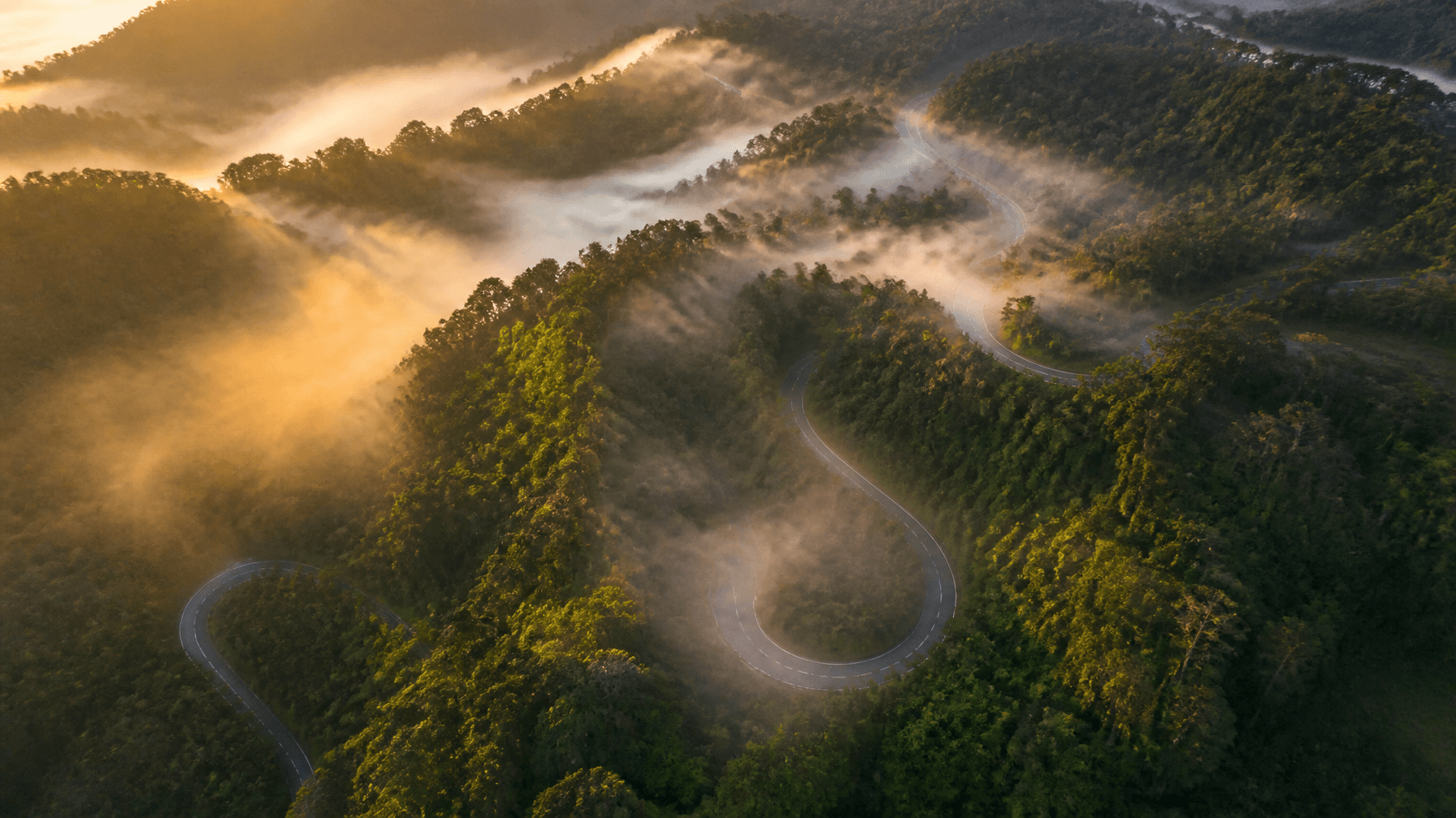 A breathtaking aerial view of winding mountain roads through lush green forests in Baturraden, Purwo